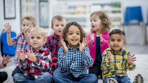Groupf young children sat down clapping in a nursery setting