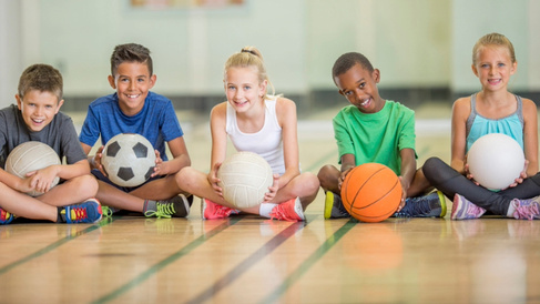Children sat in a line with different sports balls