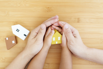 Big pair of hands holding small pair of hands holding a toy house