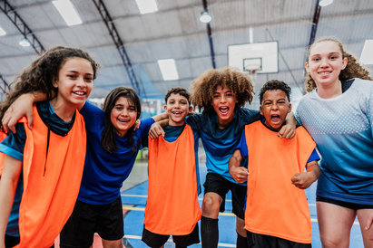Mixed group of boys and girls wearing orange bibs stood on a sports court