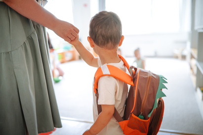 Mother holding child's hand while leading into a childcare setting