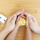 Big pair of hands holding small pair of hands holding a toy house
