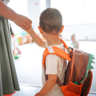 Mother holding child's hand while leading into a childcare setting