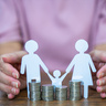 Paper stick people holding hands behind pile of coins