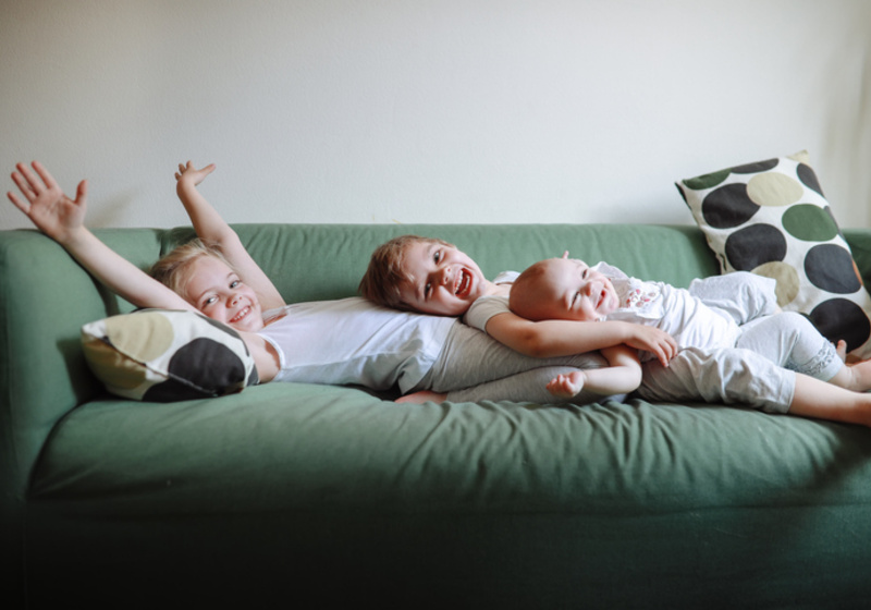 Different age siblings laying together on a sofa