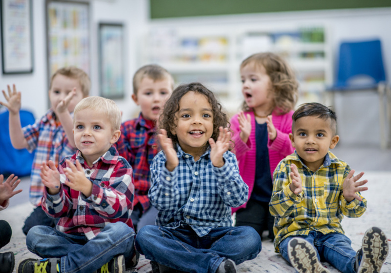 Groupf young children sat down clapping in a nursery setting